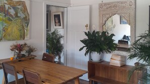 Comedor con mesa y sillas de madera, rodeado de plantas en macetas y un espejo decorativo.