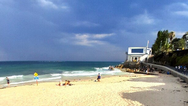 Una playa con un edificio blanco, orilla arenosa y olas del océano.