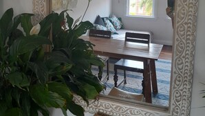 Una habitación con un espejo grande y ornamentado que refleja un comedor con una mesa, sillas, una planta en maceta y un otoman con estampado.