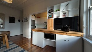 Una cocina moderna con armarios blancos, encimera de madera y horno empotrado. Hay un gato sobre la encimera, y la cocina da a una zona de comedor con mesa y sillas de madera.