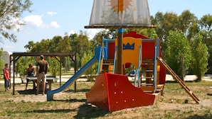 A playground with a slide, climbing structures, and a sail-shaped playhouse.