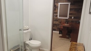 Ein Badezimmer mit Duschkabine aus Glas, Toilette und einer hölzernen Sitzbank.