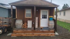 Eine kleine Holzhütte mit einem Willkommensschild, einer Tür und je zwei Fässern auf beiden Seiten.