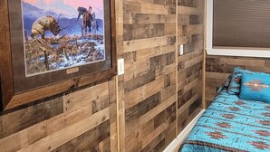 Ein Zimmer mit einer Holzwand, einem an der Wand montierten Fernseher, einem Bett mit blauen, gemusterten Bettbezügen und einem Deckenventilator.
