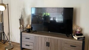 Ein modernes Wohnzimmer mit einem Flachbildfernseher auf einer Holzkommode, einer Stehlampe und dekorativen Accessoires.