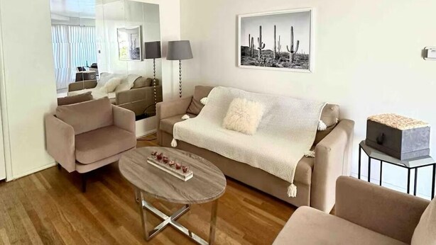 Ein modernes Wohnzimmer mit einer Couch, Sesseln, einem Couchtisch und einem gerahmten Bild an der Wand.