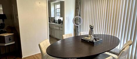 A dining area with a round table, white upholstered chairs, and a chandelier.