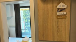 Una habitació d'hotel amb un llit, un estenat groc i vista a l'exterior a través d'una finestra.