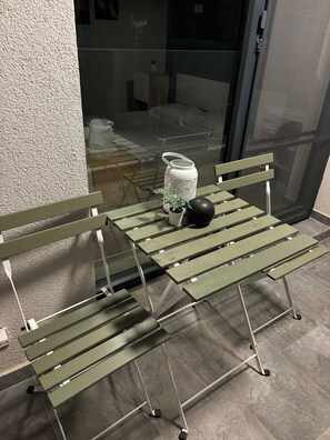 Pieni ulkotila, jossa on pöytä ja kaksi tuolia, ruukussa oleva kasvi ja koristeellinen lyhty.