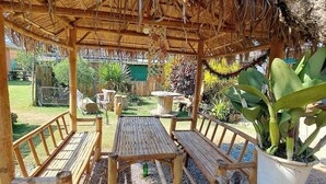 A wooden pergola with a thatched roof, wooden benches, and a table in a garden setting.