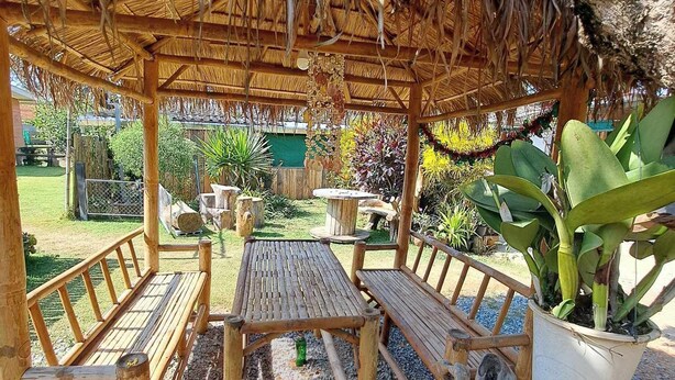 A wooden pergola with a thatched roof, wooden benches, and a table in a garden setting.