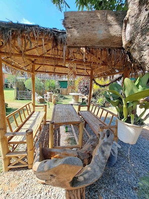 A wooden pergola with a thatched roof, wooden benches, and a table in a garden setting.