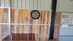 A room with a wooden table, a dartboard, and a calendar on the wall.