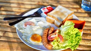 A plate with eggs, sausages, lettuce, and toast on a wooden table.