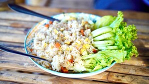 A plate of fried rice with vegetables and a side of lettuce on a wooden table.