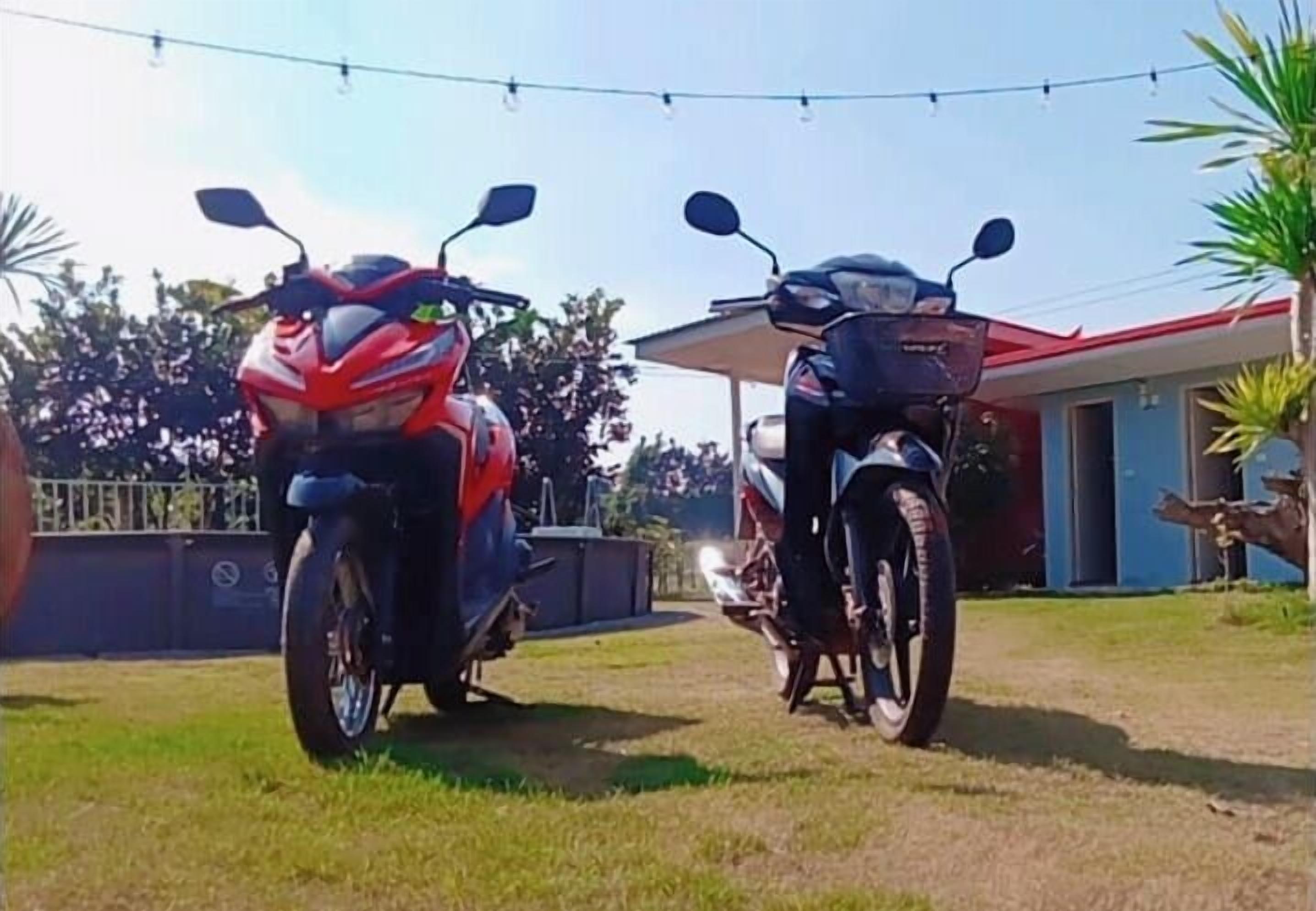 Two motorcycles parked in a grassy area with a building in the background.