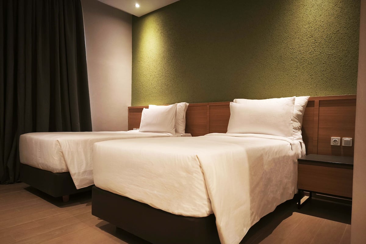 A hotel room with two beds, a wooden headboard, a green textured wall, and a wooden floor.