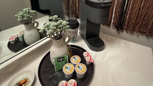 A bathroom with a sink, a coffee maker, a mirror, and a decorative vase with artificial flowers.