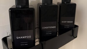 A black shelf with three bottles of personal care products: shampoo, conditioner, and body wash.