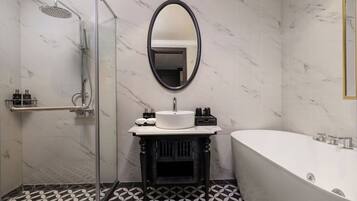 A bathroom with a glass-enclosed shower, a round mirror, a sink with a marble countertop, and a freestanding bathtub.