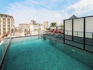 Piscina infinita en la azotea con agua azul cristalina, barandilla de vidrio y vistas a la ciudad.