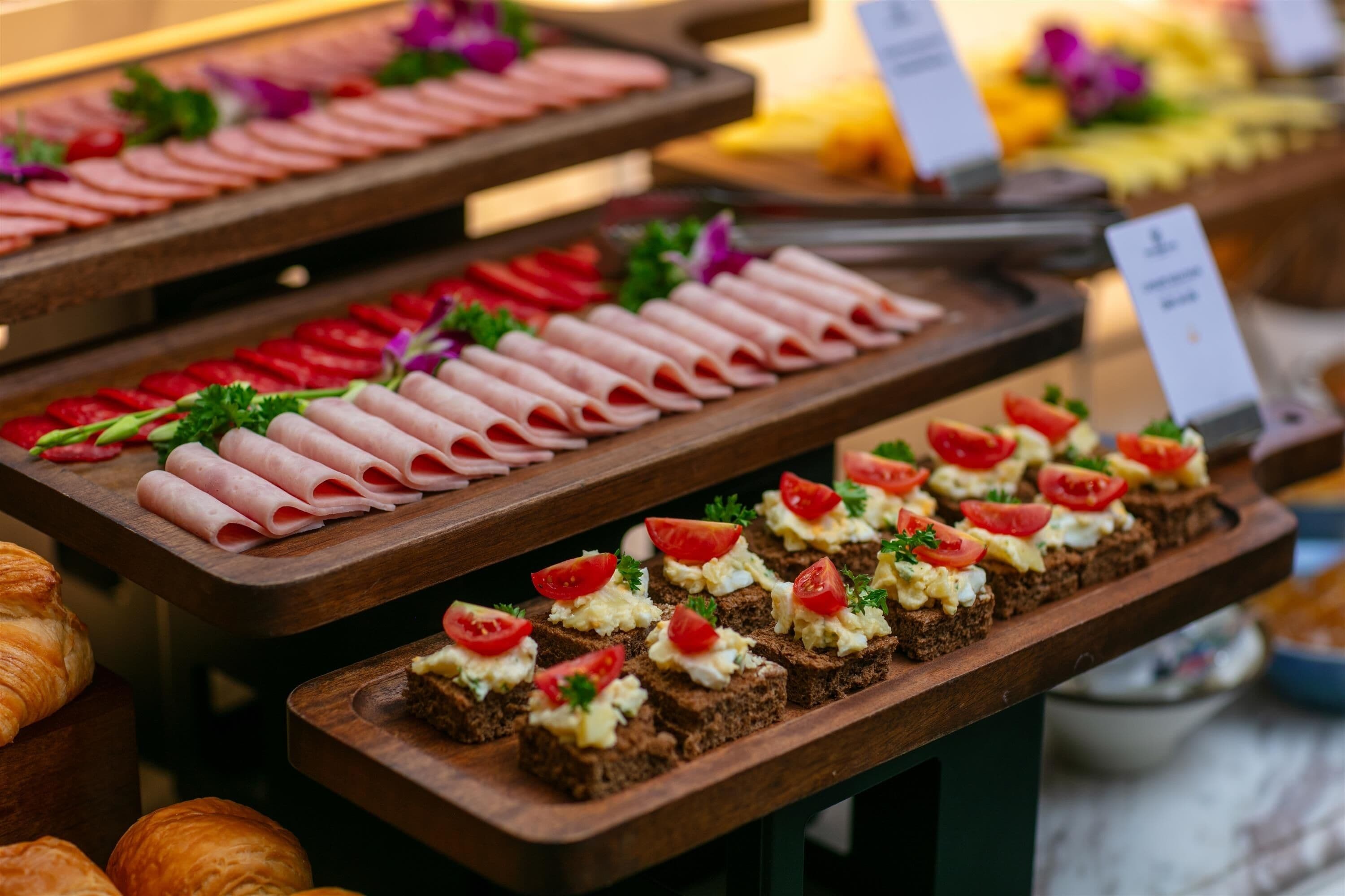 A buffet with various food items including sliced meats, tomatoes, and bread.