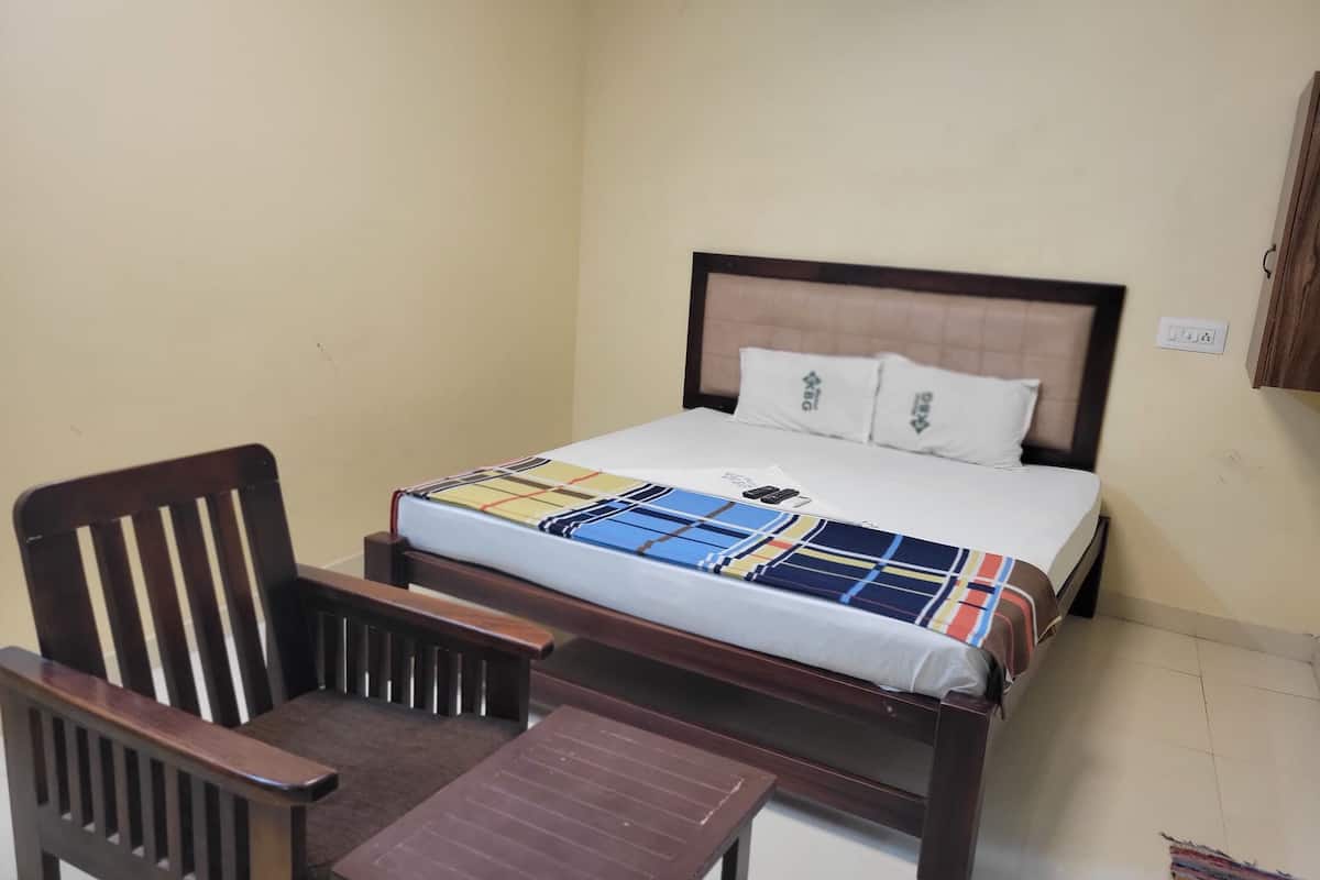 Un dormitorio con una cama, una silla de madera, una mesita pequeña y una manta colorida.