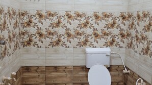 Een badkamer met toilet, douche en een blauwe emmer.