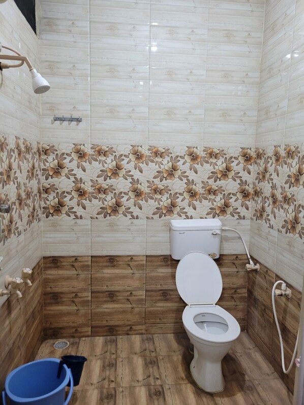 Une salle de bain avec des toilettes, une douche et un seau bleu.