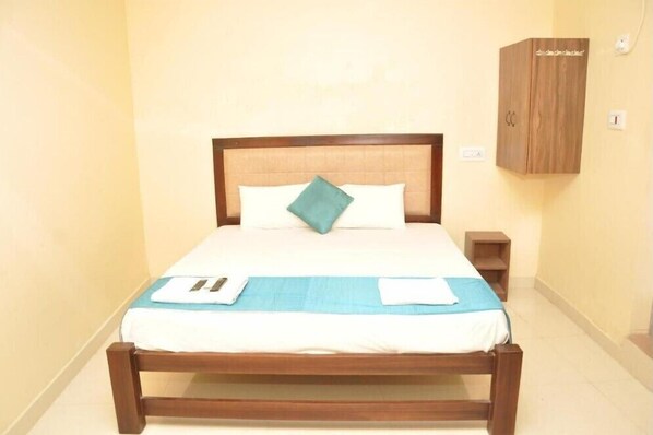A neatly made bed with a wooden frame, a blue bedspread, and a teal pillow. There is a small wooden nightstand beside the bed.