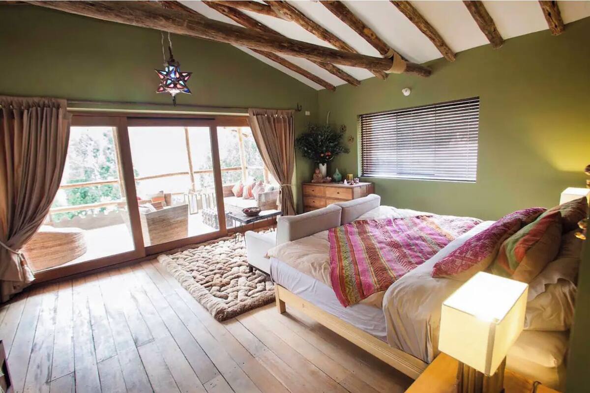 A bedroom with a large bed, wooden flooring, a star-shaped hanging light, and a view of the outdoors through a sliding door.