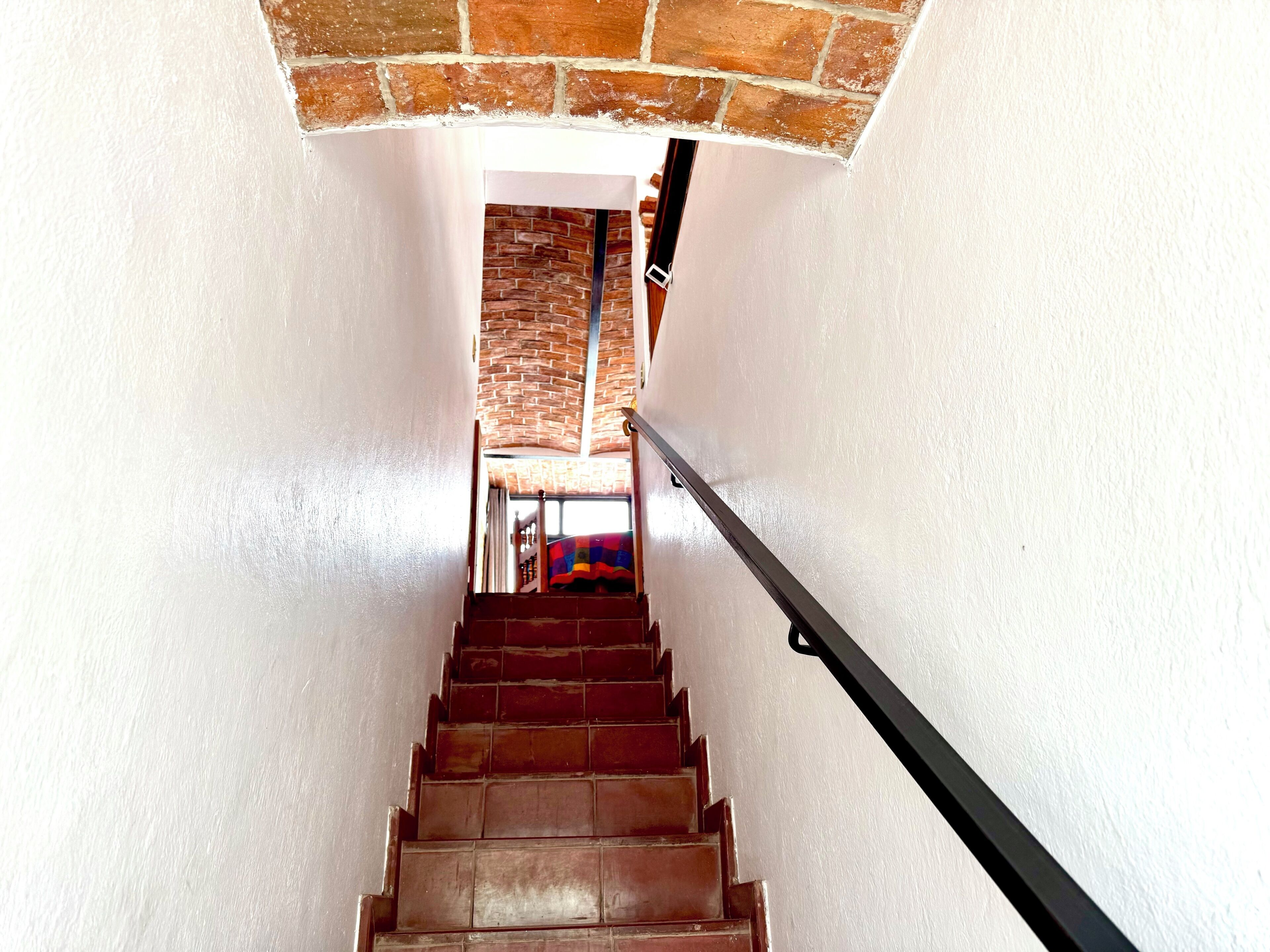 A staircase with a brick wall at the top, a metal handrail, and a colorful rug at the bottom.