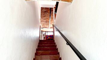 A staircase with a brick wall at the top, a metal handrail, and a colorful rug at the bottom.