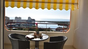 Un balcon agrémenté de fauteuils en osier, une petite table sur laquelle est posé un vase de fleurs, et une vue sur une marina et les bâtiments situés de l’autre côté de l’eau.