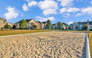 Un terrain de beach-volley sablonneux, avec un filet, entouré d’immeubles d’habitation.