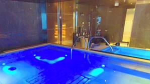 Una amplia piscina interior con suelo iluminado en azul, rodeada de paredes de vidrio y un diseño interior moderno.