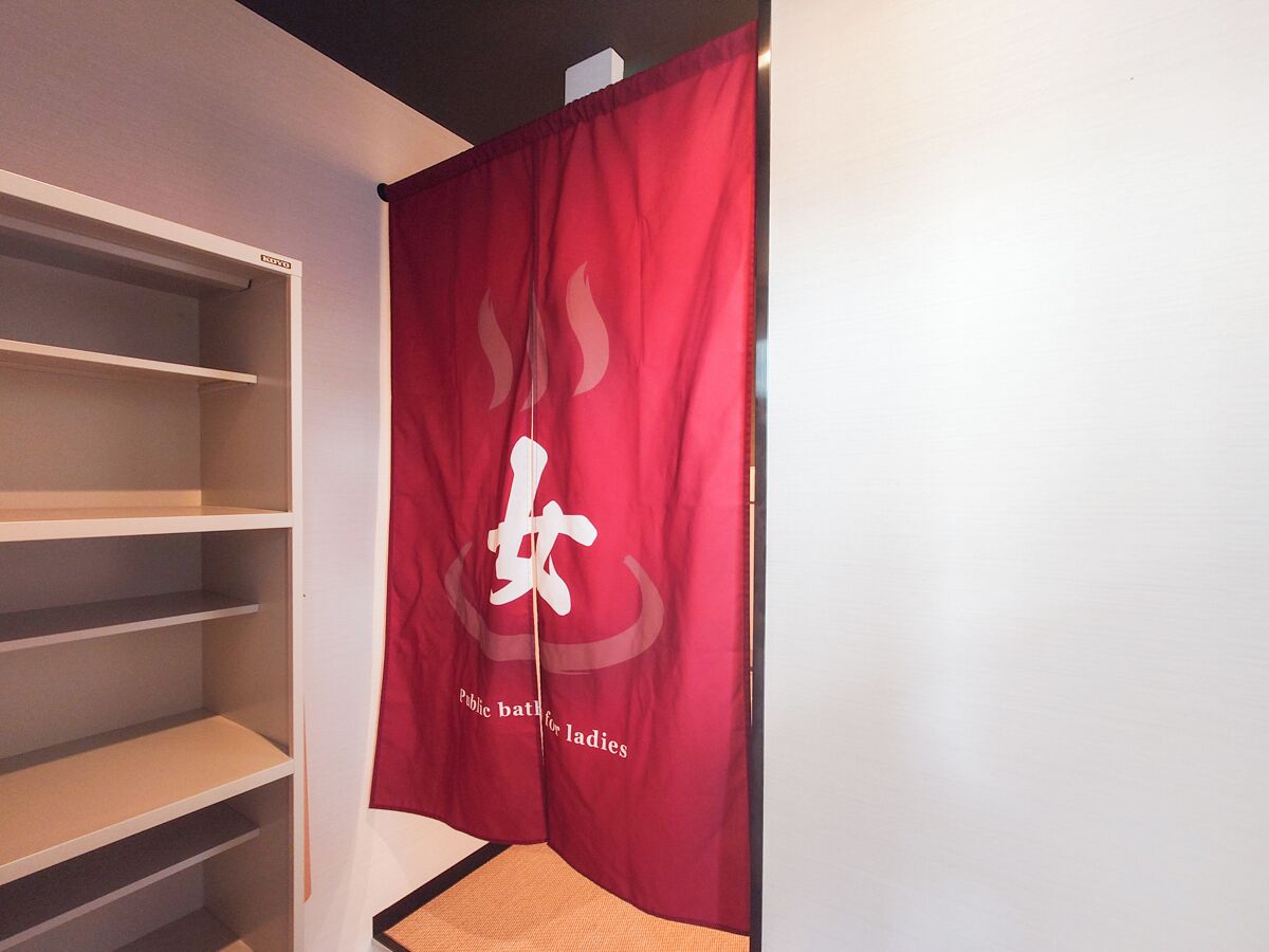 Um quarto com uma faixa vermelha pendurada na parede, uma estante branca e uma pequena mesa de madeira.