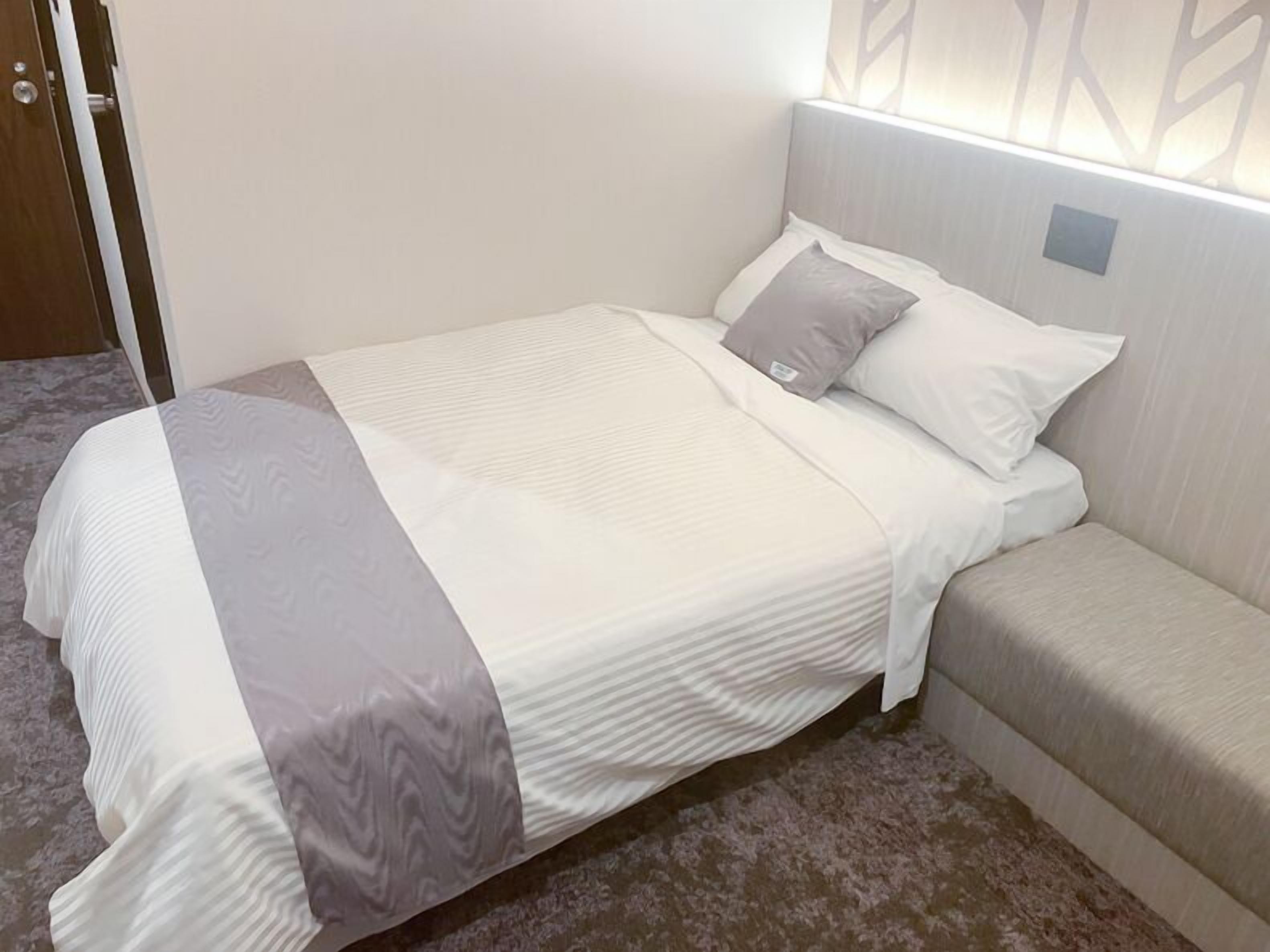 A neatly made bed with a white and grey bedspread, a grey pillow, and a grey headboard.