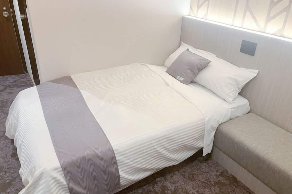 Una cama bien hecha con una colcha blanca y gris, un almohadón gris y un cabecero gris.