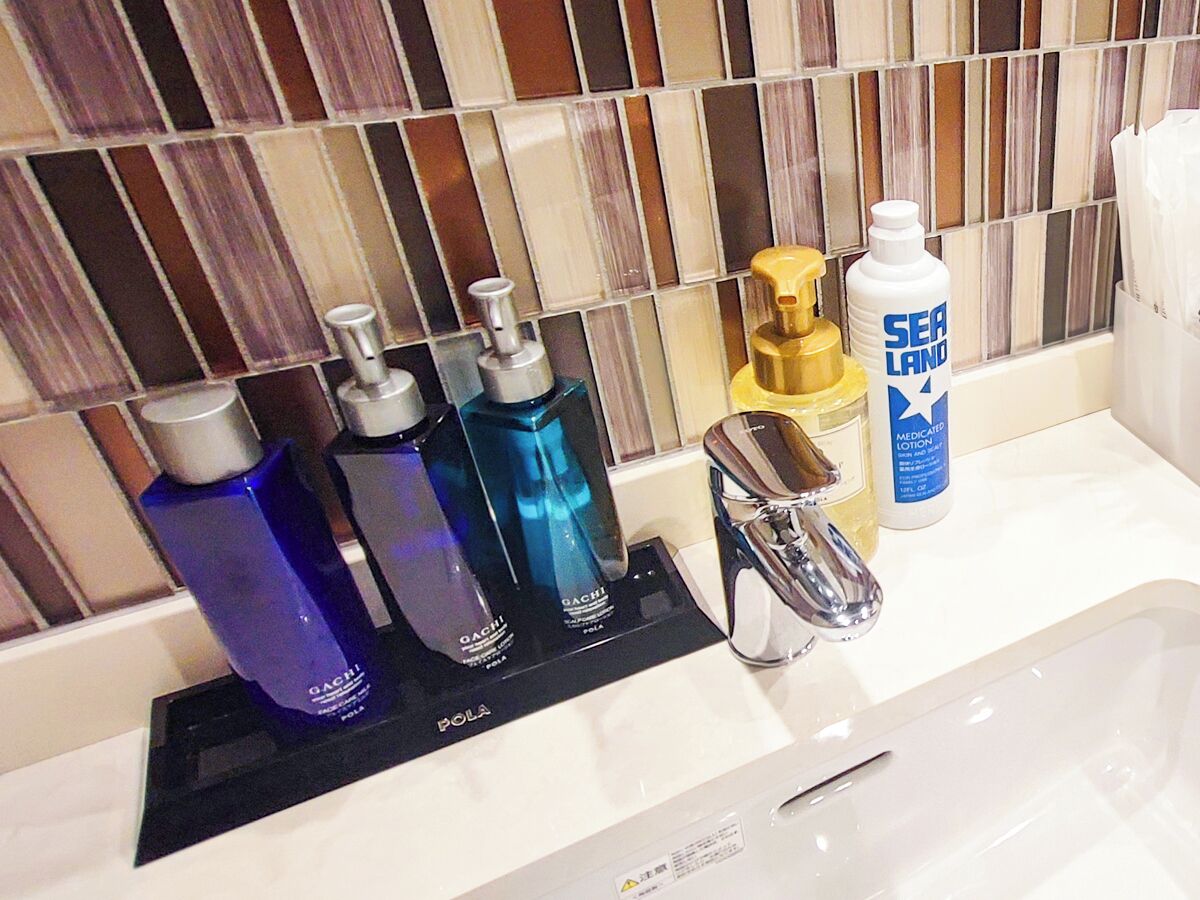 A bathroom with a modern design, featuring a tiled backsplash, a sink with a chrome faucet, and three toiletry bottles on a black tray.