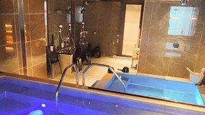 Una piscina interior moderna con una barrera de cristal, una escalera metálica y un elemento acuático iluminado en azul.