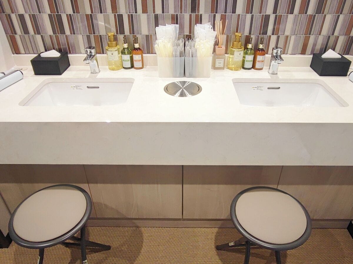 A bathroom with two sinks, a mirror, and two stools.