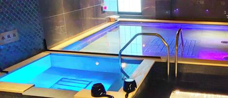 Una piscina interior moderna con fondo de cristal, dos porselanas negras en el borde y una escalera metálica que conduce a la piscina.