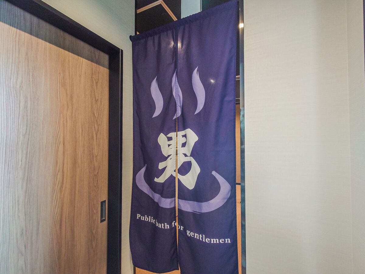 Een kamer met een houten deur en een paarse banner met een logo en de tekst 'Publicbath for gentlemen'.