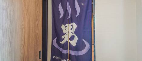 A room with a wooden door and a purple banner with a logo and text reading "Publicbath for gentlemen".