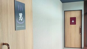 Un baño público con un letrero que indica que es para caballeros, una puerta de madera y suelo de madera.
