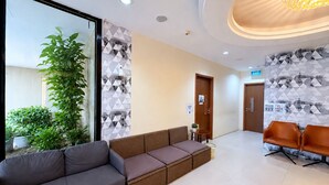 Un espace d’accueil avec un canapé, des fauteuils, une plante en pot et un papier peint à motifs.