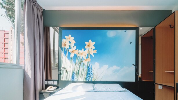 Une chambre d’hôtel avec un grand lit, une table de chevet, un téléphone et une fresque florale sur le mur.