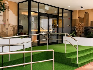 A hotel lobby with a glass facade, a staircase with metal railings, and a green artificial turf area. - Amrise Hotel Geylang, 11Hrs Stay from 10PM to 9AM (Singapore)