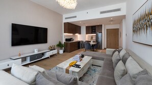 Una sala moderna con un televisor de pantalla plana grande, un sofá, una mesa de centro y un comedor con una cocina al fondo.